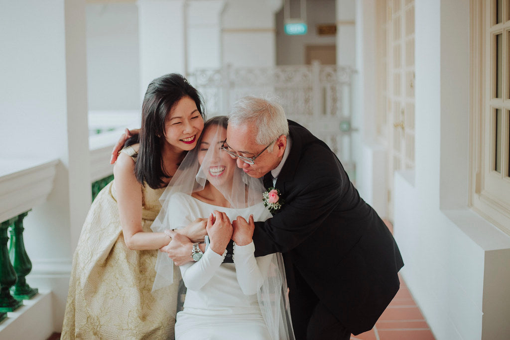 Bride wearing a bespoke WeddingCrafters gown sharing a joyful moment with her family on her wedding day in Singapore.