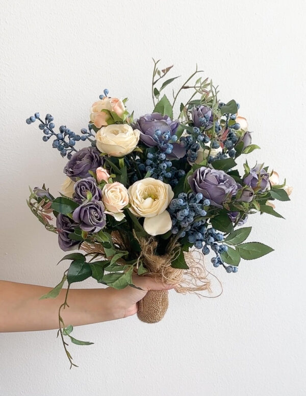 Bouquet of flowers with purple, white, and green colors held by a person against a white background