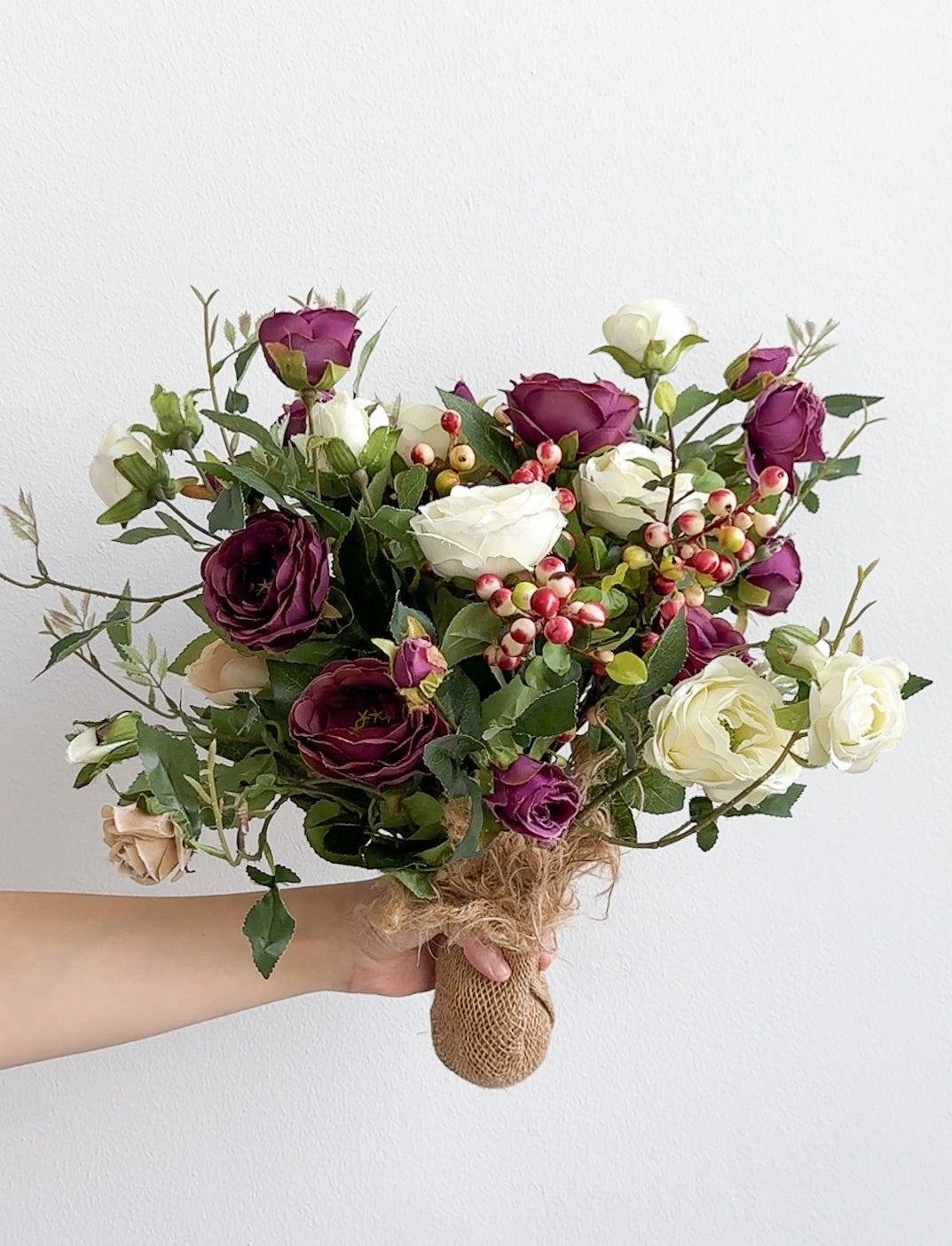 Bouquet of flowers with purple and white roses held by a hand against a white background