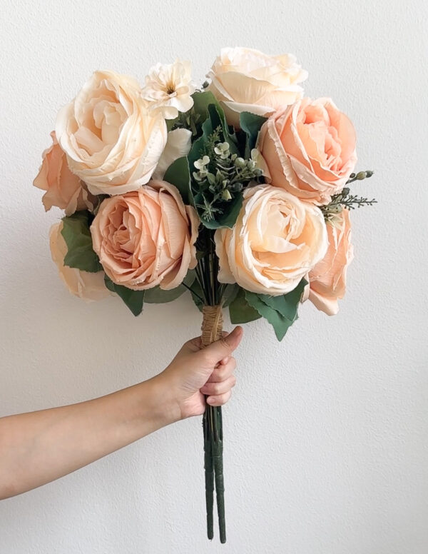 Bouquet of peach-colored roses held by a hand against a white background