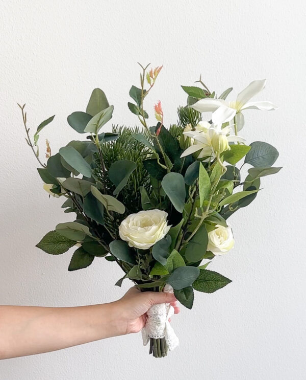 Bouquet of greenery and white flowers held by a hand against a light background